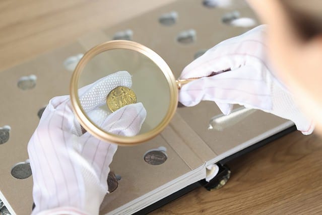 Close-up of woman numismatist examining coin with magnifier. Female looks at coins through loupe. Numismatic collection review