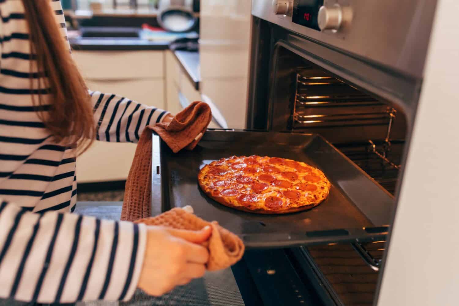 Female hands put pepperoni pizza in oven