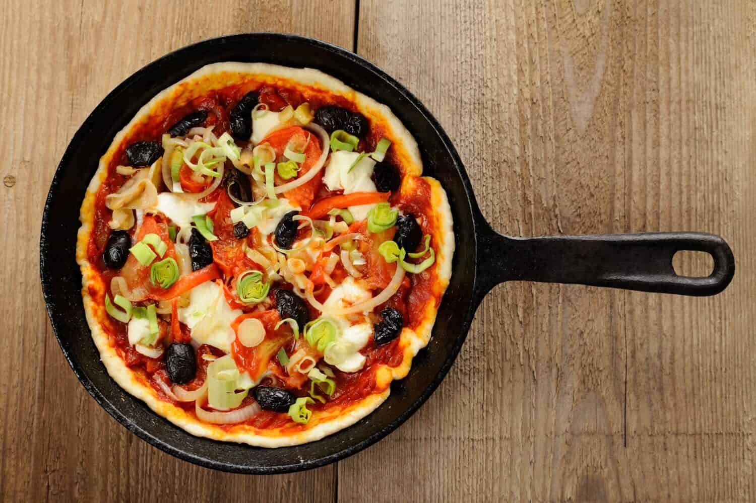 Raw pizza with olives and salmon in cast iron skillet