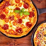Two fresh pan pizzas on iron skillets , wooden background , top view