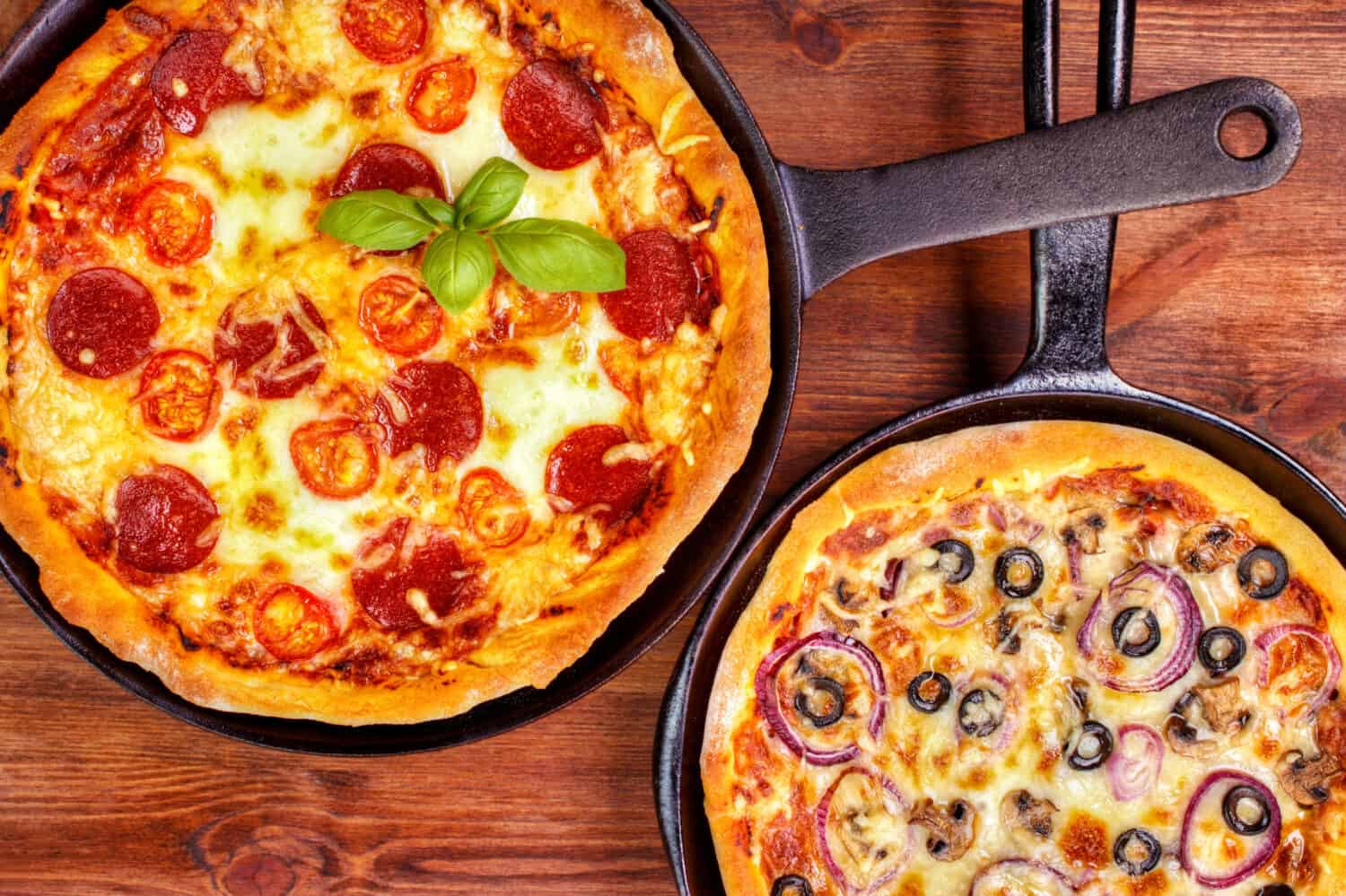 Two fresh pan pizzas on iron skillets , wooden background , top view