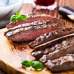 Well-done grilled marinated beef flank steak on wooden board