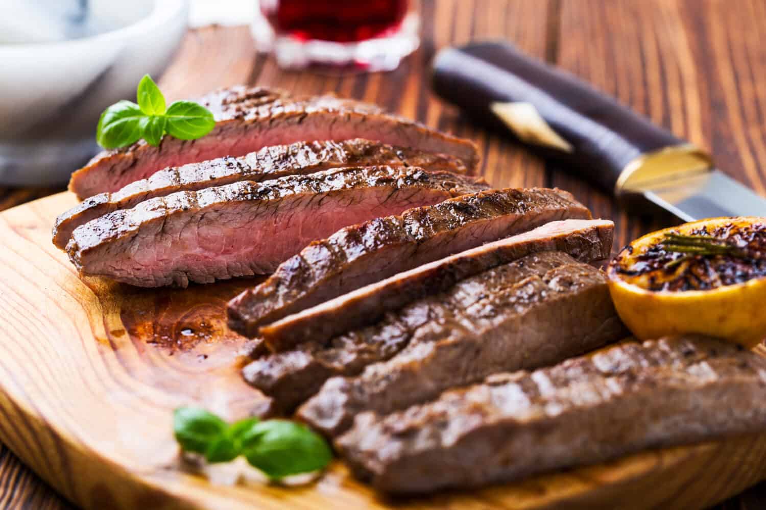 Well-done grilled marinated beef flank steak on wooden board