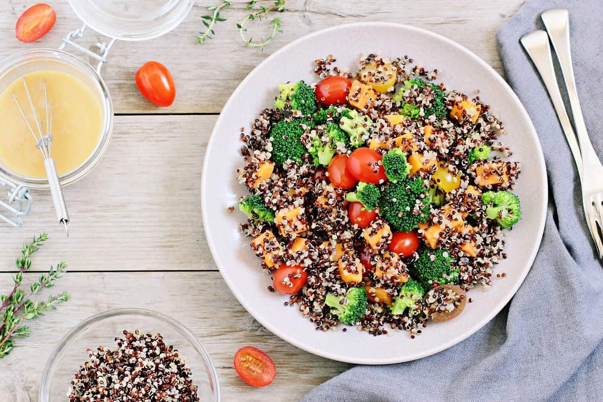 Quinoa salad with broccoli, sweet potatoes and tomatoes on a rustic wooden table. Three-color quinoa salad. Superfood and healthy eating concept.