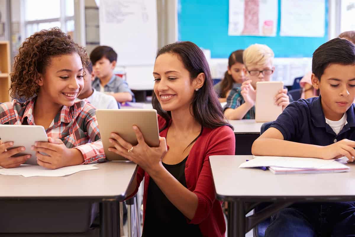 A teacher aiding a pupil on how to use a tablet in class.