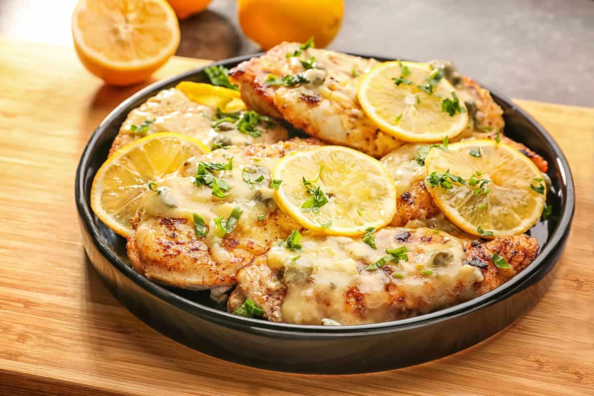 Plate with delicious chicken piccata on wooden board
