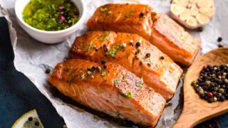Delicious fried salmon fillet, seasonings on blue rustic concrete table. Cooked salmon steak with pepper, herbs, lemon, garlic, olive oil, spoon. Grilled fresh fish. Fish for healthy dinner. Close-up