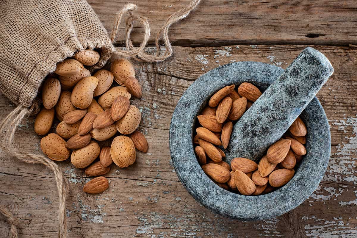 Many almonds in the stone mortar and sack bag.