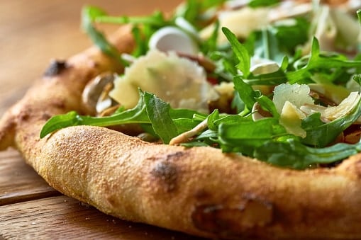 Vegetarian wood-fired pizza with arugula, vegetables and parmesan on wood board. Selective focus