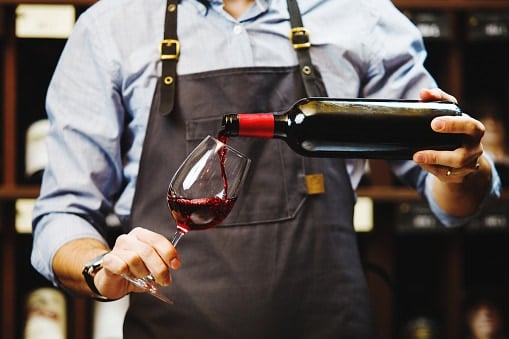 Male sommelier pouring red wine into long-stemmed wineglasses.