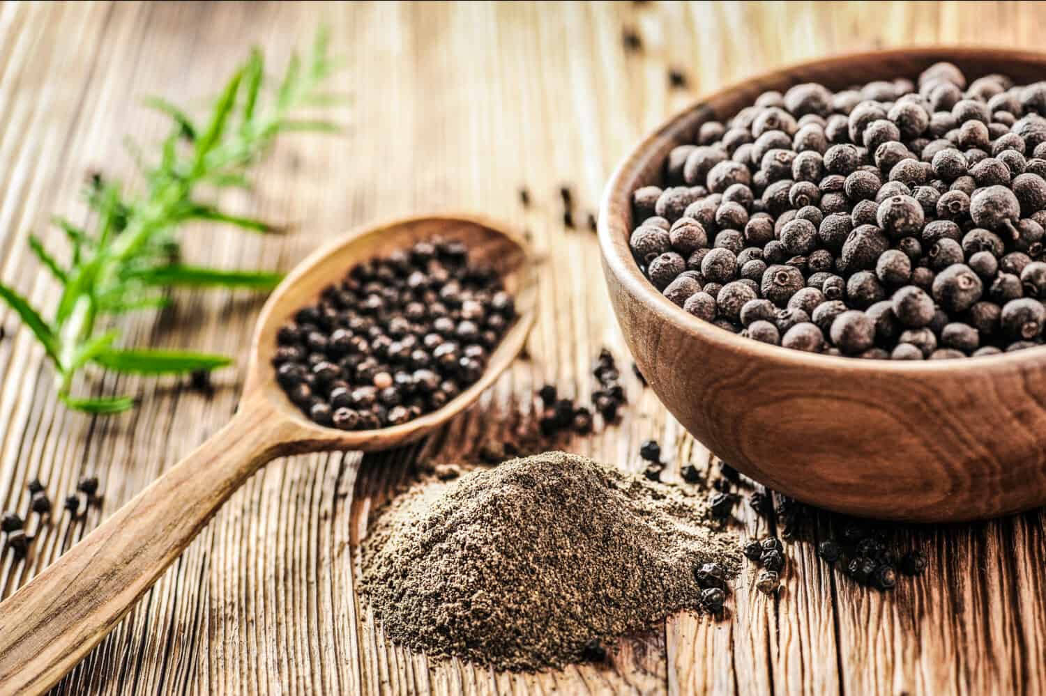 Black pepper in bow on wooden table. Pile of ground black pepper.