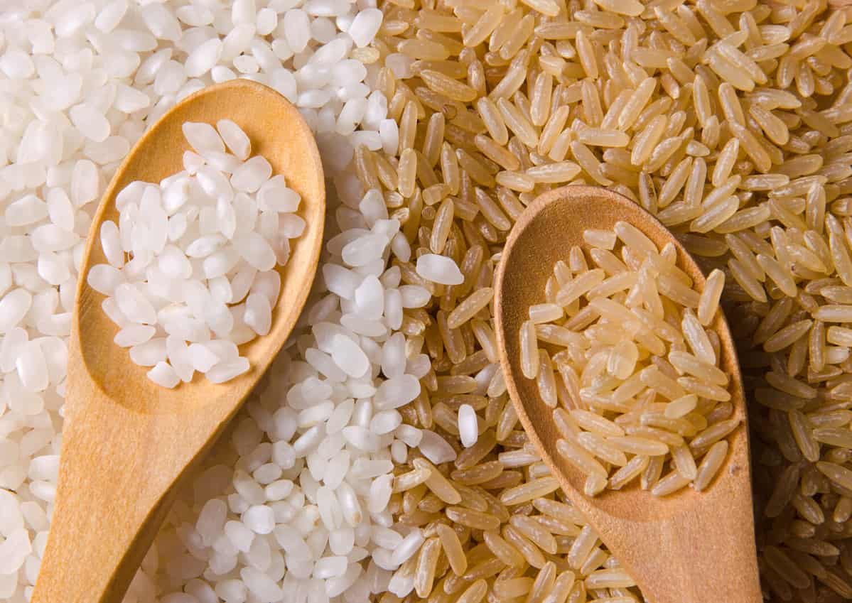 Natural white and brown long rice in wood spoons.