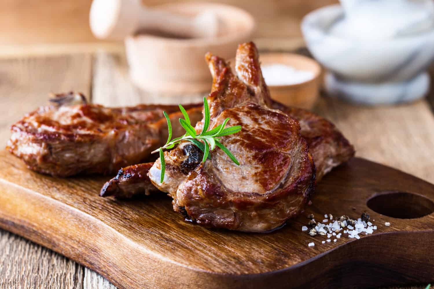 Roasted veal chops with fresh herbs on rustic wooden cutting board, pan seared steak dinner