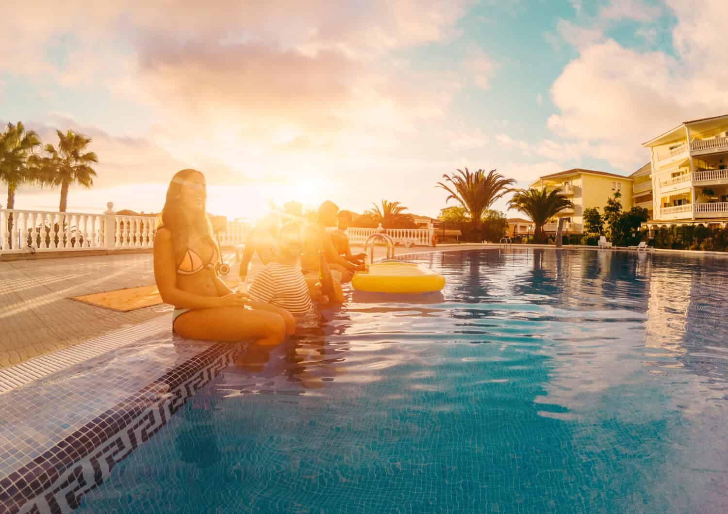 Happy friends drinking champagne in pool party at sunset - Rich people having fun in exclusive tropical vacation - Summer holiday, youth lifestyle and friendship concept