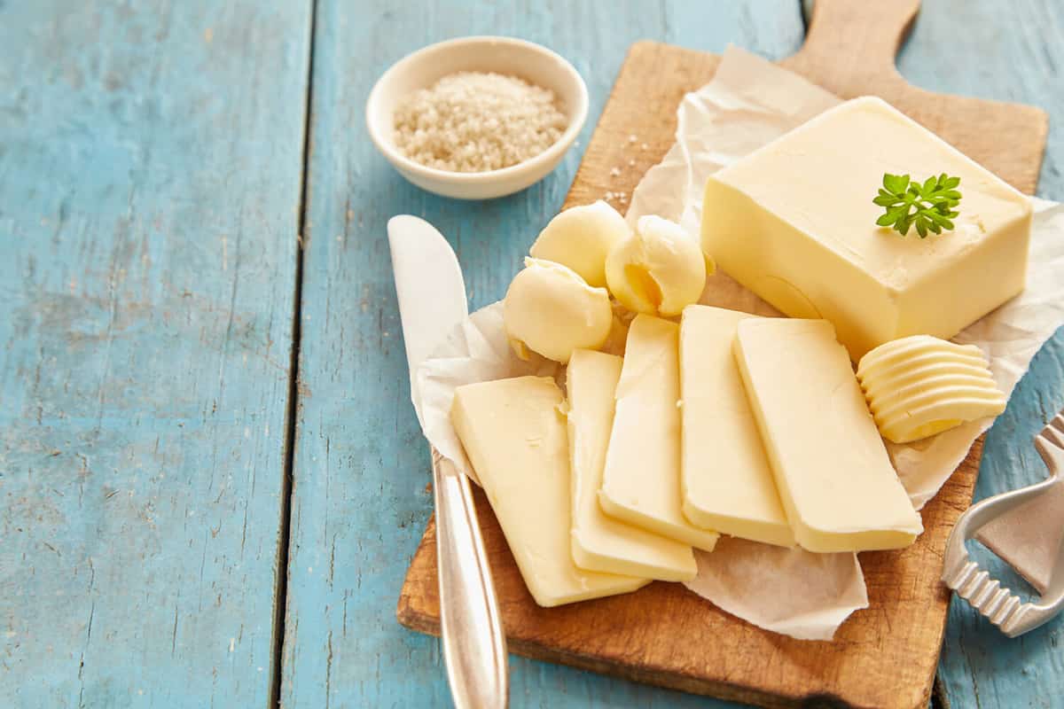 Block of fresh butter sliced on wooden cutting board against blue table