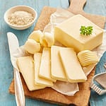 Block of fresh butter sliced on wooden cutting board against blue table