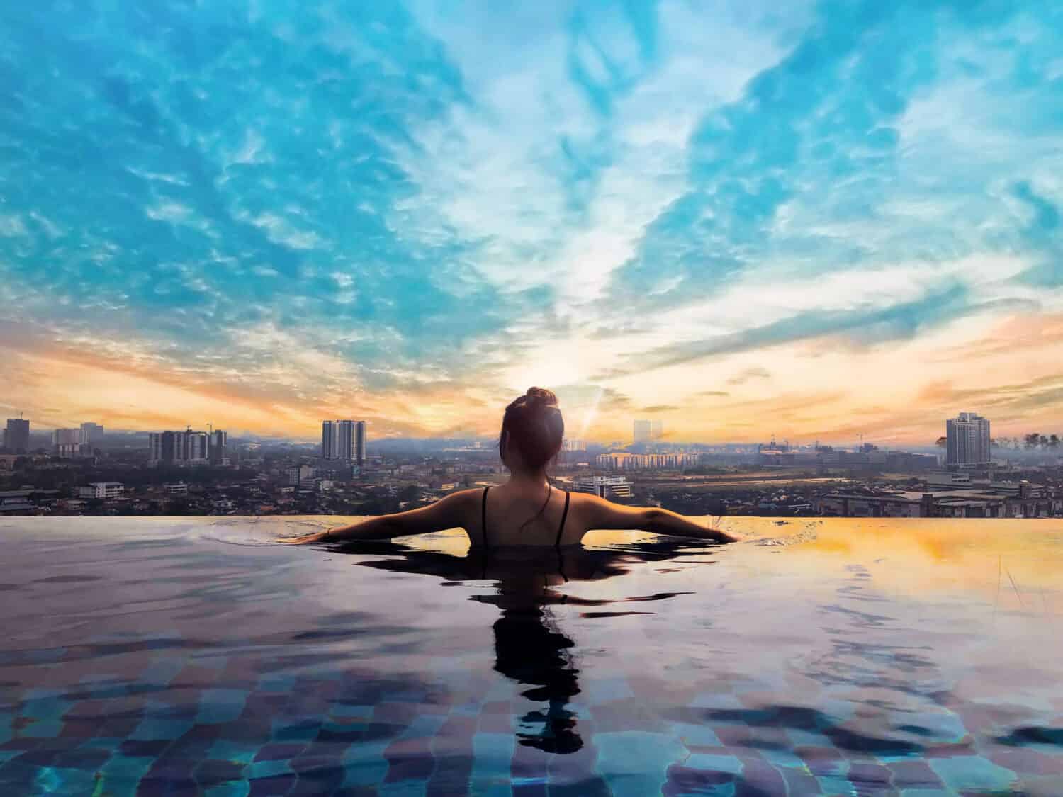 Woman relaxing in infinity pool with city view. Relaxing vacation.