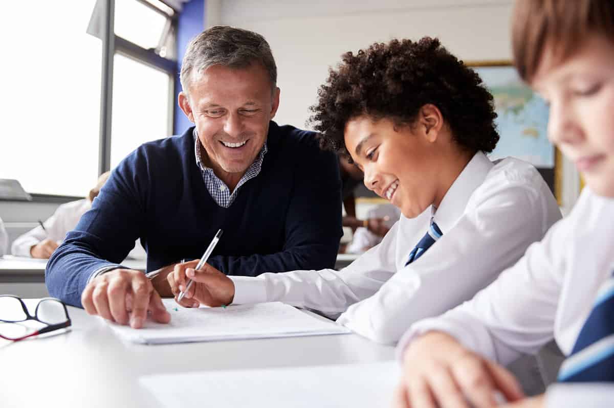 High School Tutor Giving Male Student Wearing Uniform One To One Tuition At Desk