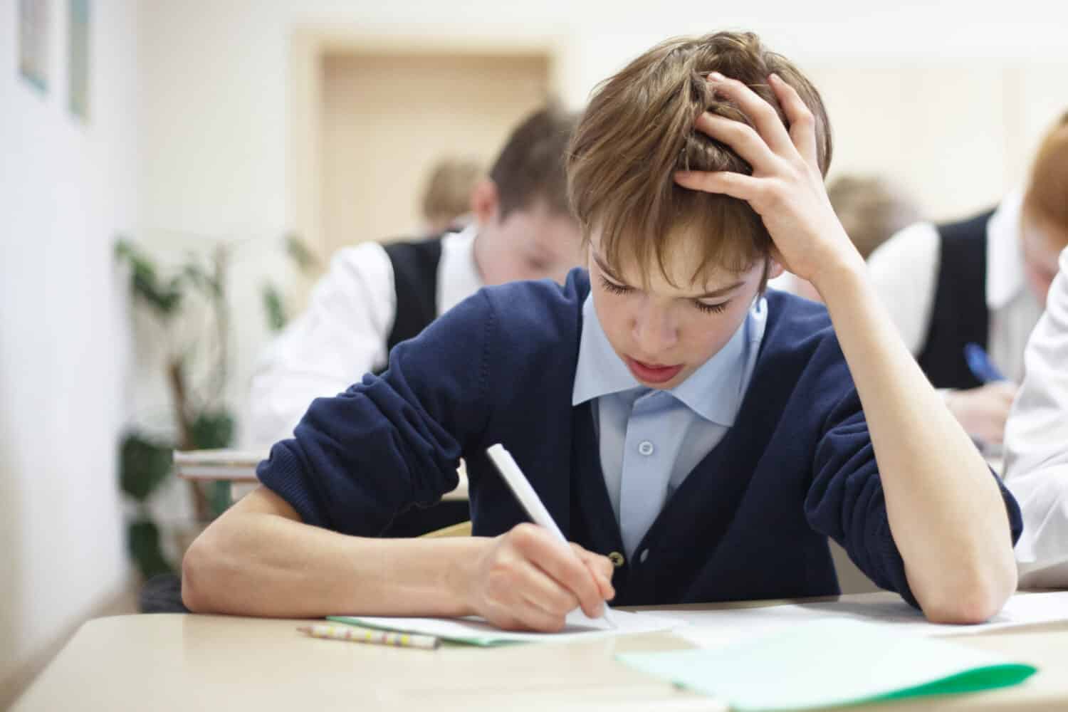 thoughtful school boy struggling to finish test in class.