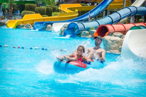 In the summer, on a bright sunny day, in a water park, father and daughter slide down the hill on an air mattress.