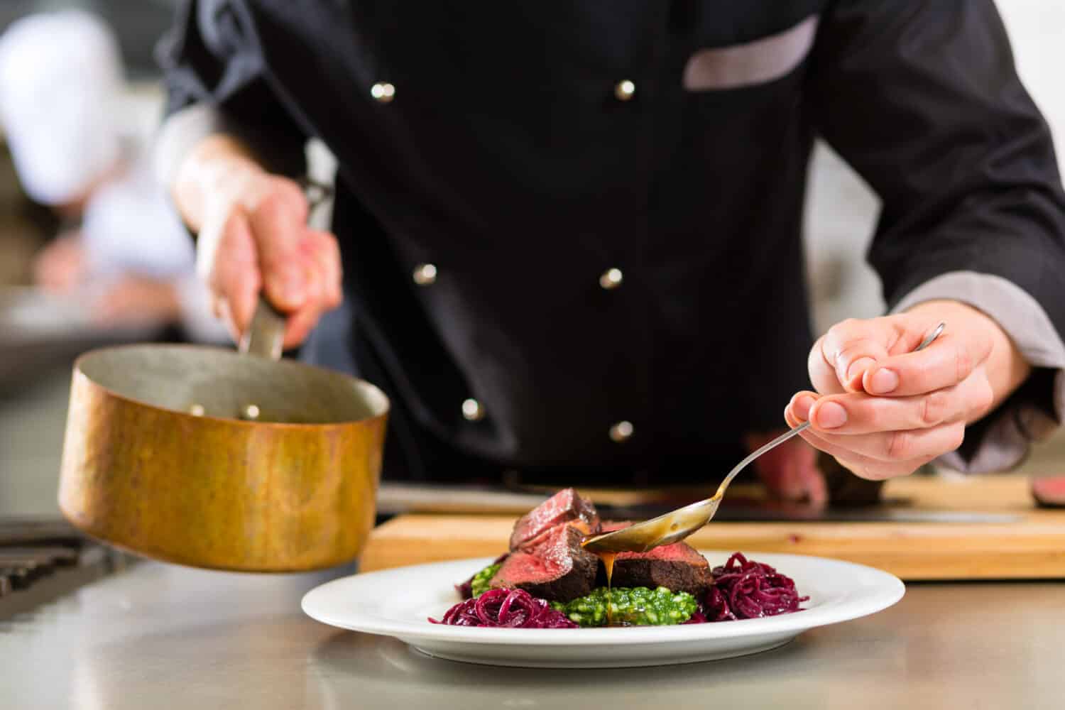 Chef in hotel or restaurant kitchen cooking, only hands, he is working on the sauce for the food as saucier, a Risotto