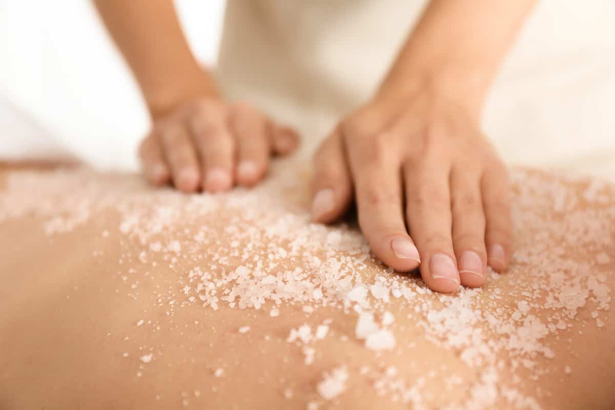 Young woman having body scrubbing procedure with sea salt in spa salon, closeup