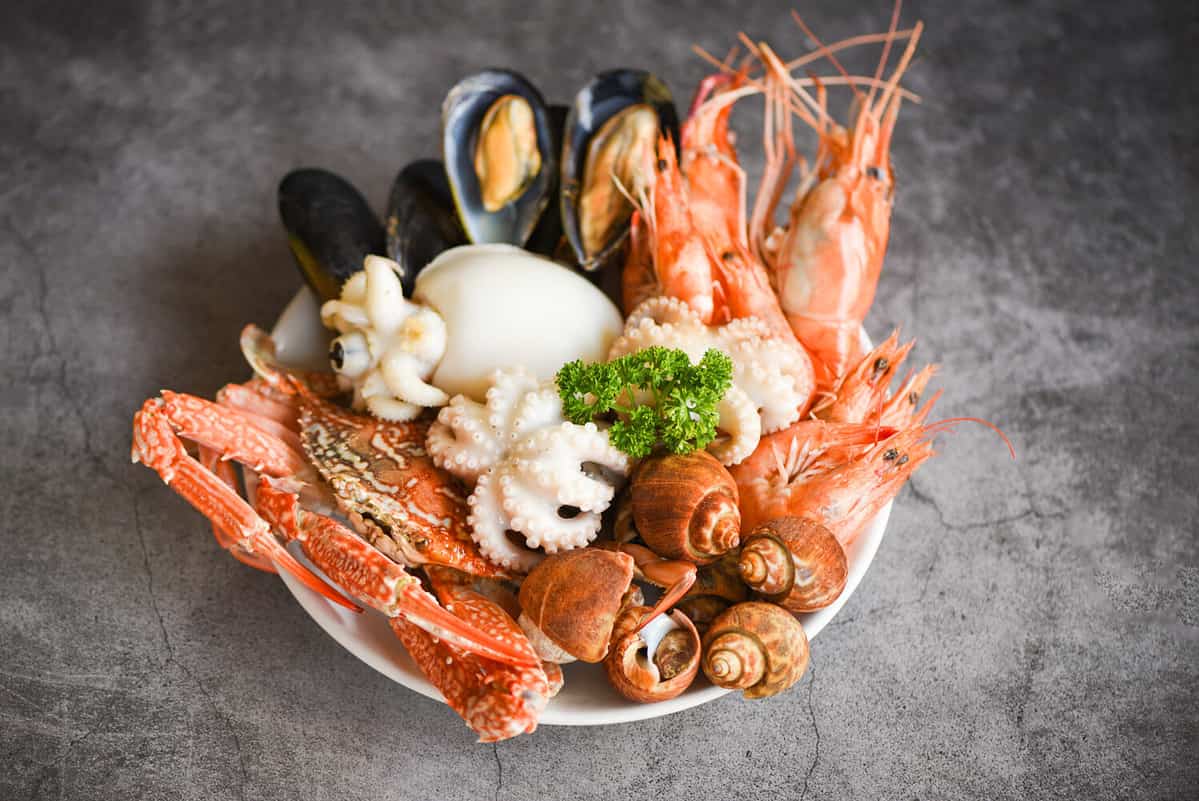 Seafood shrimps prawns squid mussels spotted babylon shellfish crab on plate and dark background / Cooked food served seafood buffet concept