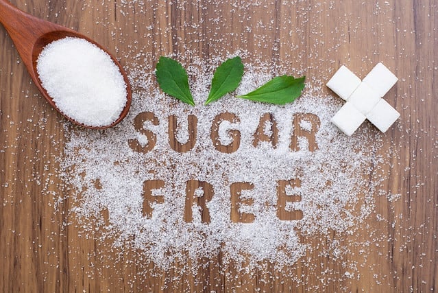 White sugar and words " sugar free " letters written in sugar grains with Stevia leaf isolated on wood table background. Sweetener concept. Top view.