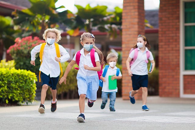 School child wearing face mask during corona virus and flu outbreak. Boy and girl going back to school after covid-19 quarantine and lockdown. Group of kids in masks for coronavirus prevention.