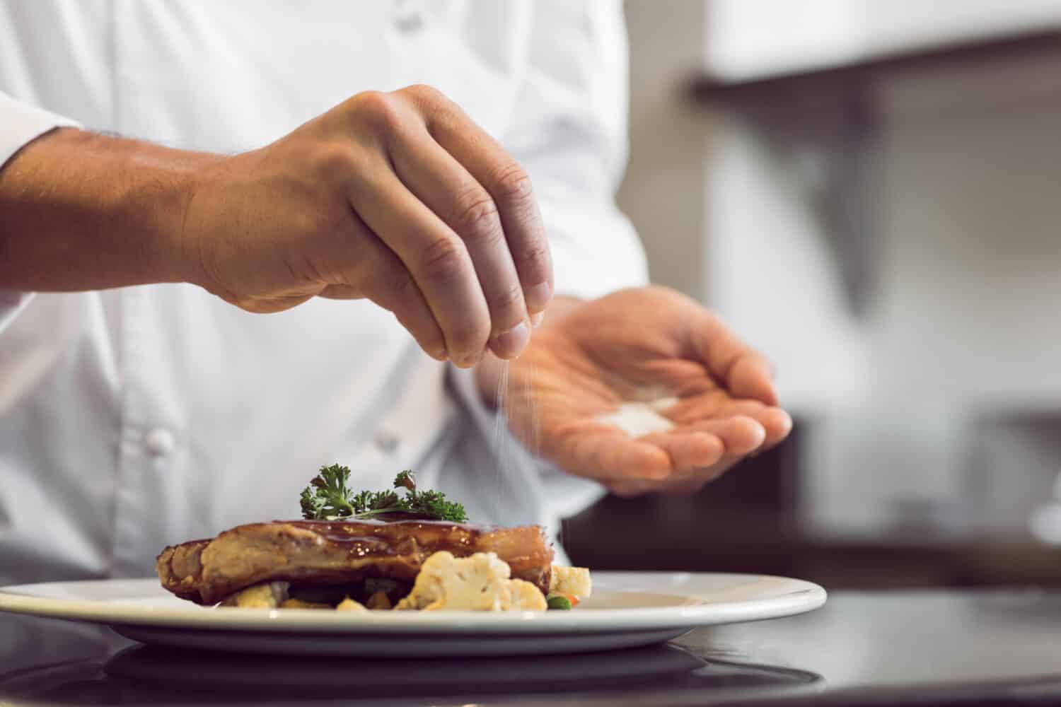 Closeup mid section of a chef putting salt in the kitchen