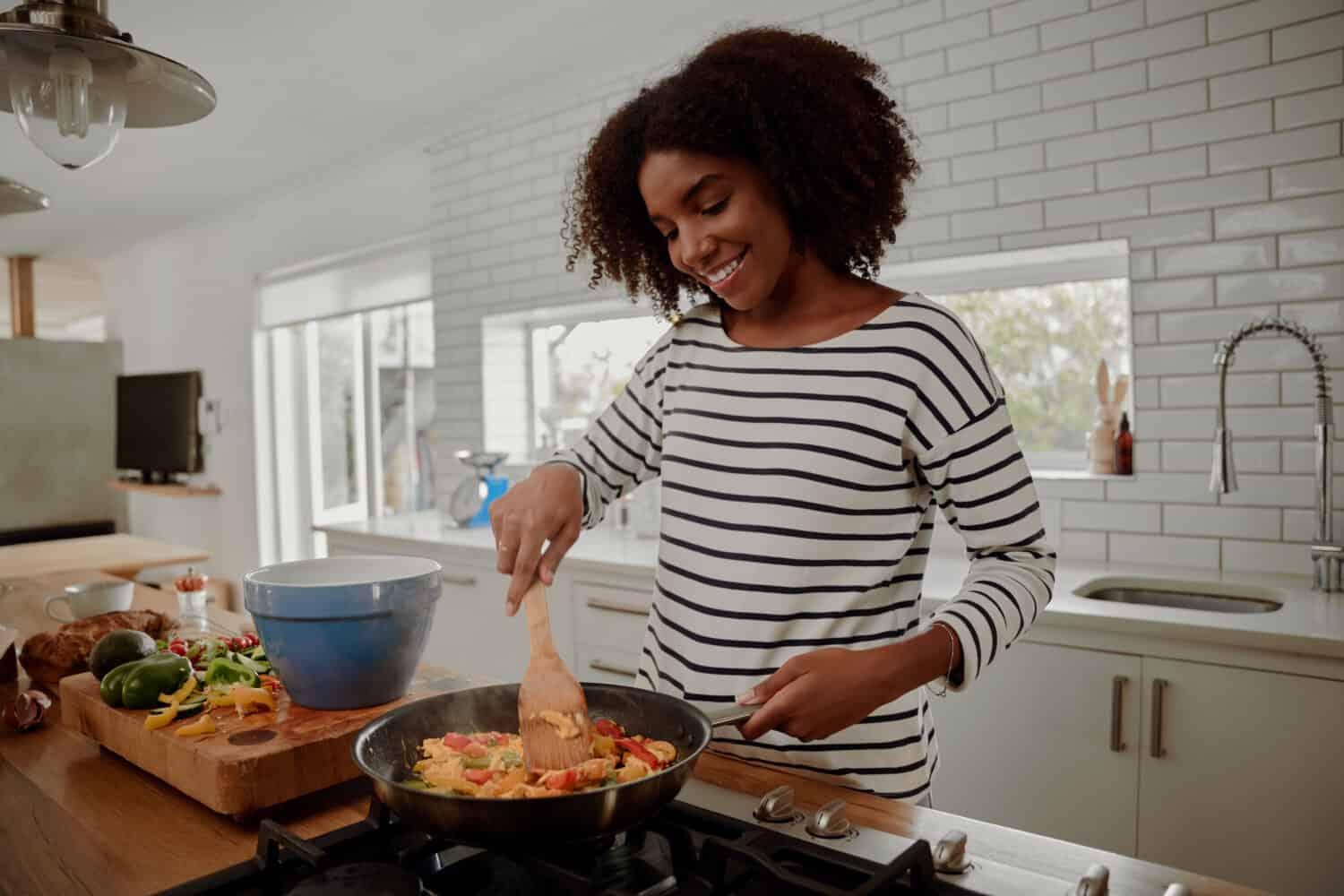 Woman mixing ingredients and vegetables in pan while preparing lunch