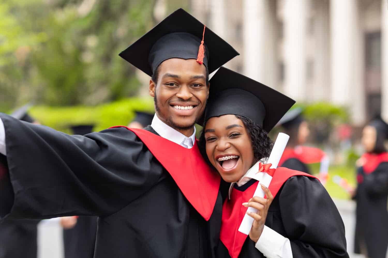 Happy african american couple students in graduation dresses and hats taking selfie together, posing at university campus, enjoying and celebrating graduation, closeup portrait