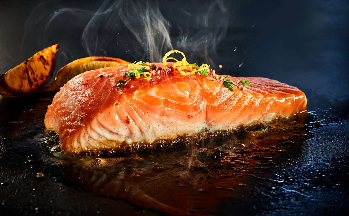 Gourmet portion of thick juicy fresh salmon grilling on a griddle seasoned with lemon zest, herbs and spices in a low angle view with copyspace and rising steam