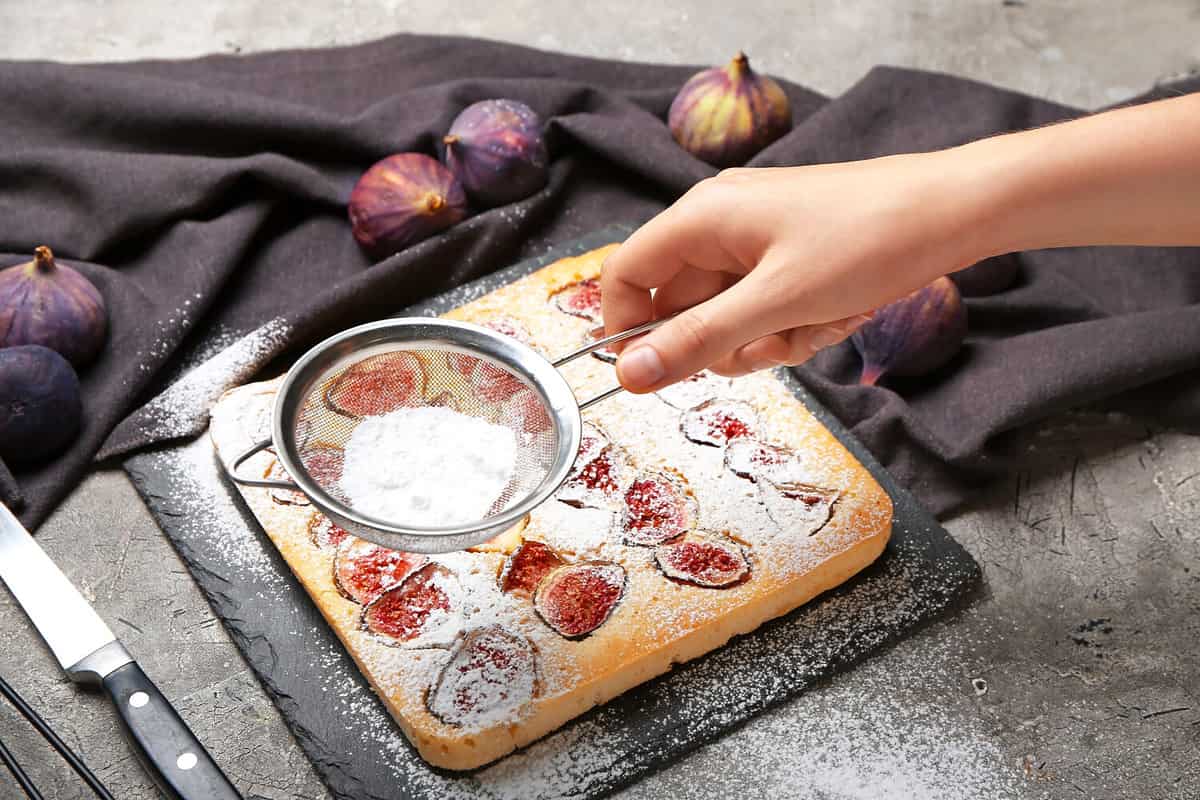 Woman sprinkling delicious fig pie with sugar powder on grunge background