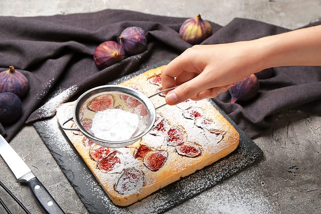 Woman sprinkling delicious fig pie with sugar powder on grunge background