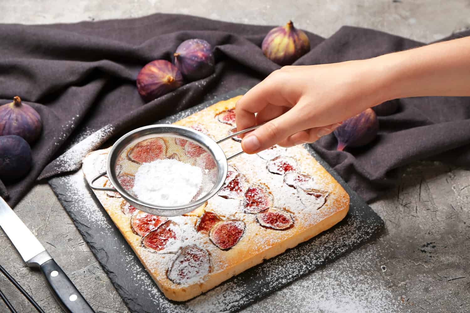 Woman sprinkling delicious fig pie with sugar powder on grunge background