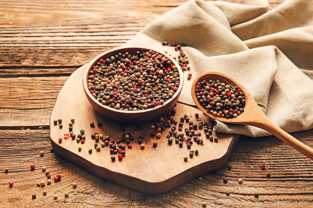 Bowl and spoon with mixed peppercorns on wooden background