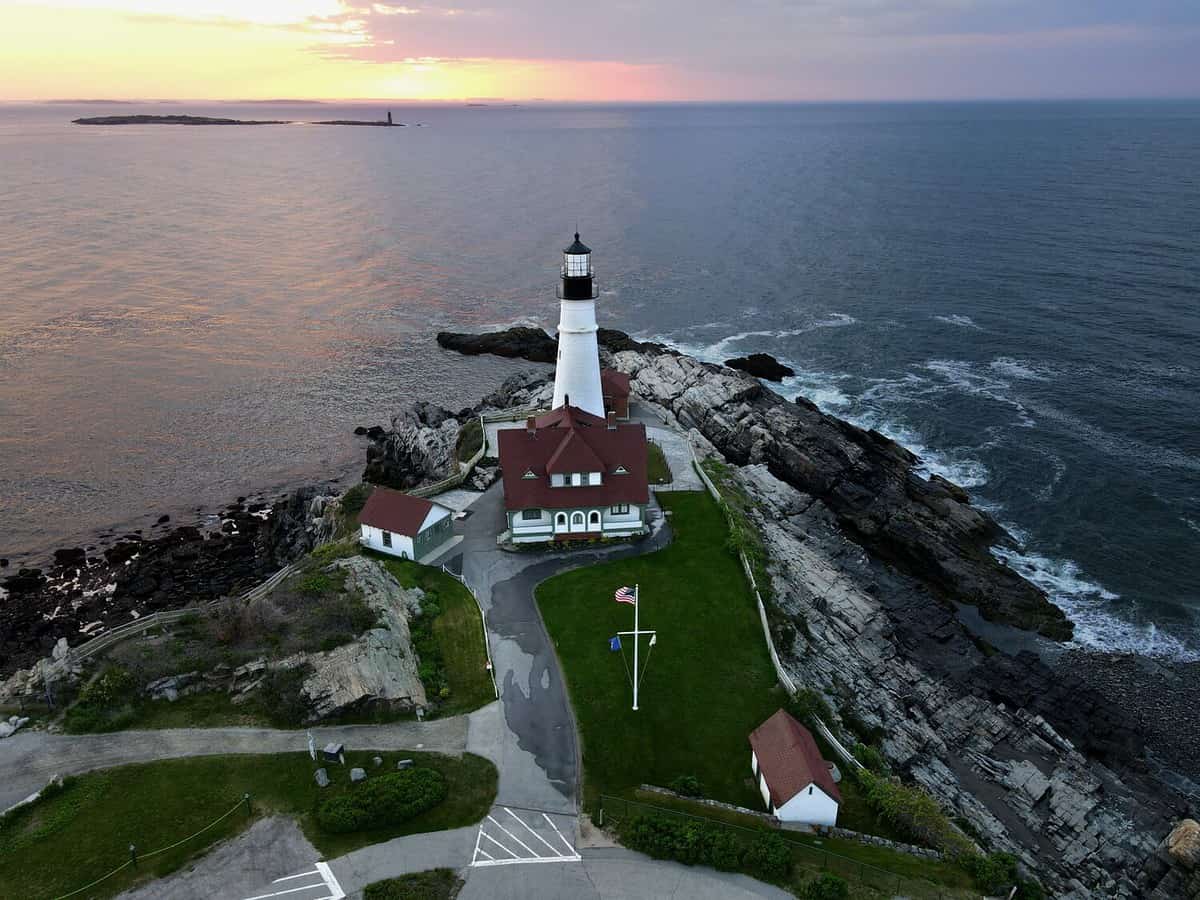 An aerial view of the Portland Headlight in Cape Elizabeth Maine guarding the Atlantic Coast as the sunrises behind it