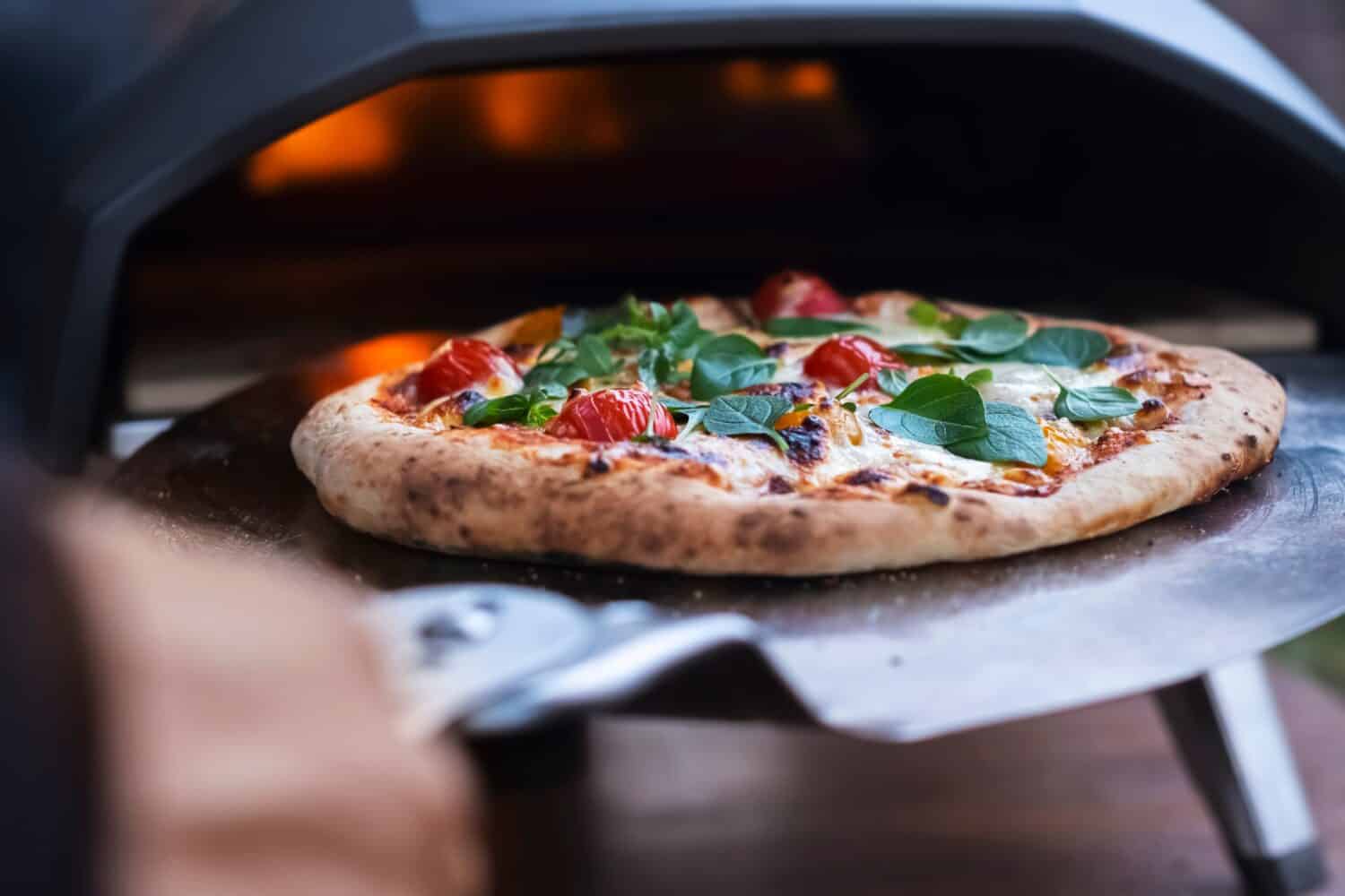 A pizza margarita with fresh basil leaves on the background of a gas oven for cooking pizza.