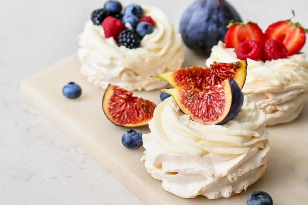Board of tasty Pavlova cakes with berries on light background, closeup