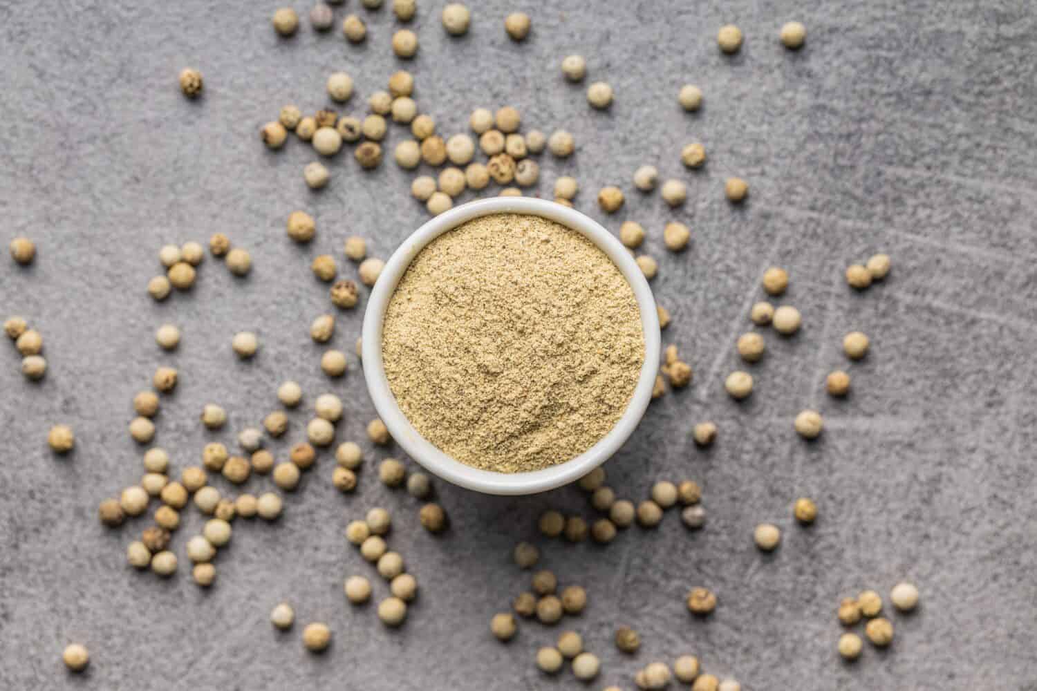 White ground pepper and whole peppercorn spice in a bowl. Top view.