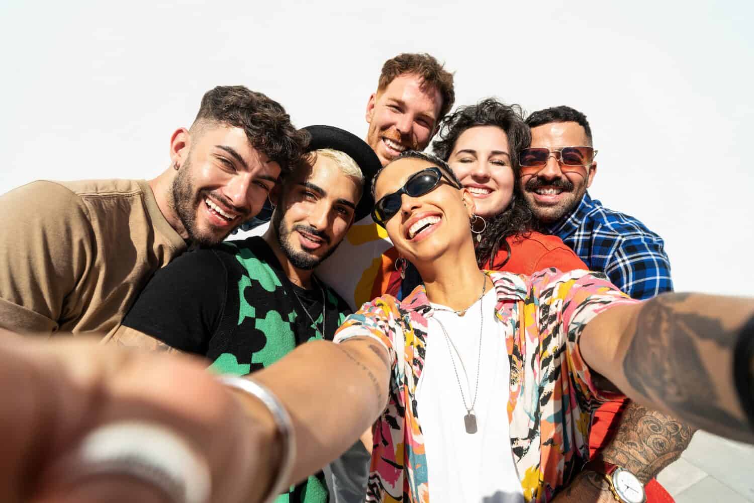 Group of happy young friends having fun and laughing while taking a selfie with mobile phone. Diverse millennial people spending time together. Friendship concept. Real people lifestyle.
