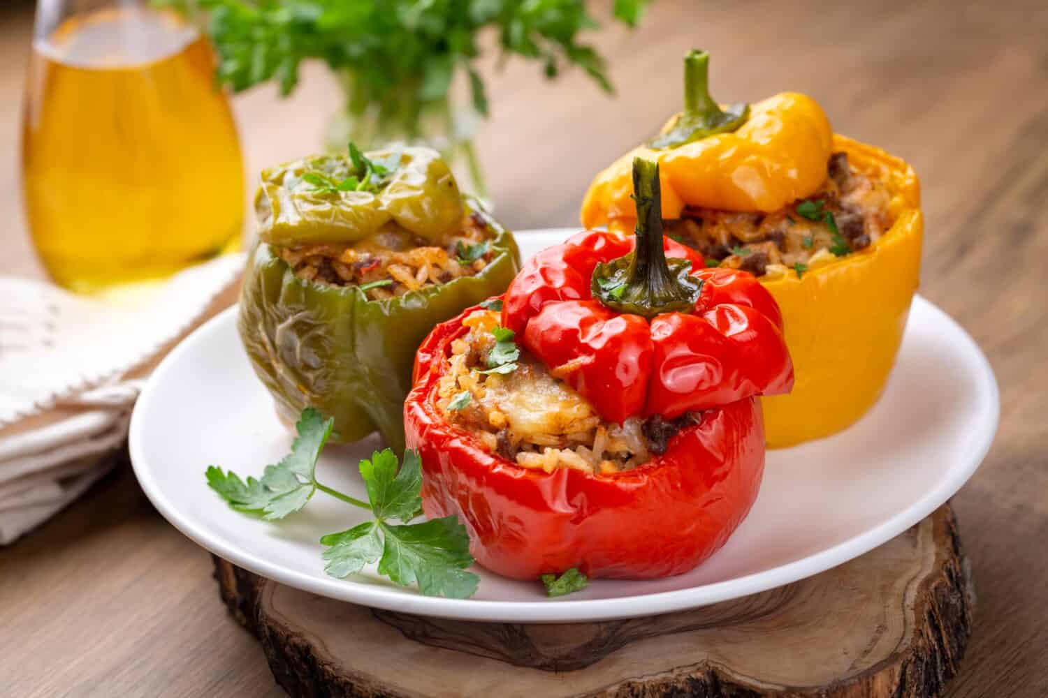 Stuffed peppers, halves of peppers stuffed with rice, dried tomatoes, herbs and cheese in a baking dish on a blue wooden table, top view. Vegetarian dish, stuffed vegetables