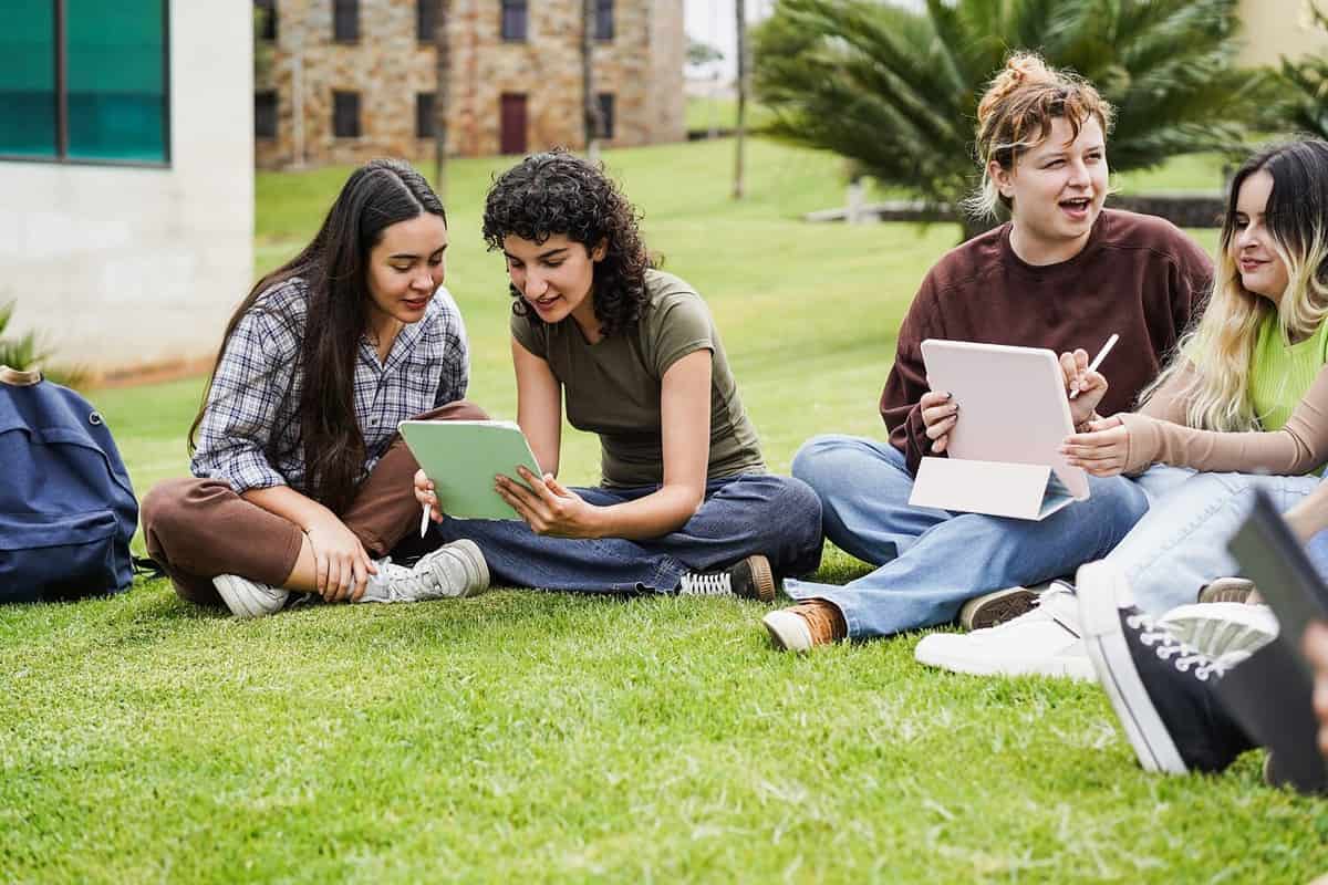 Young friends studying together outdoor sitting in university campus park - Focus on left girls faces