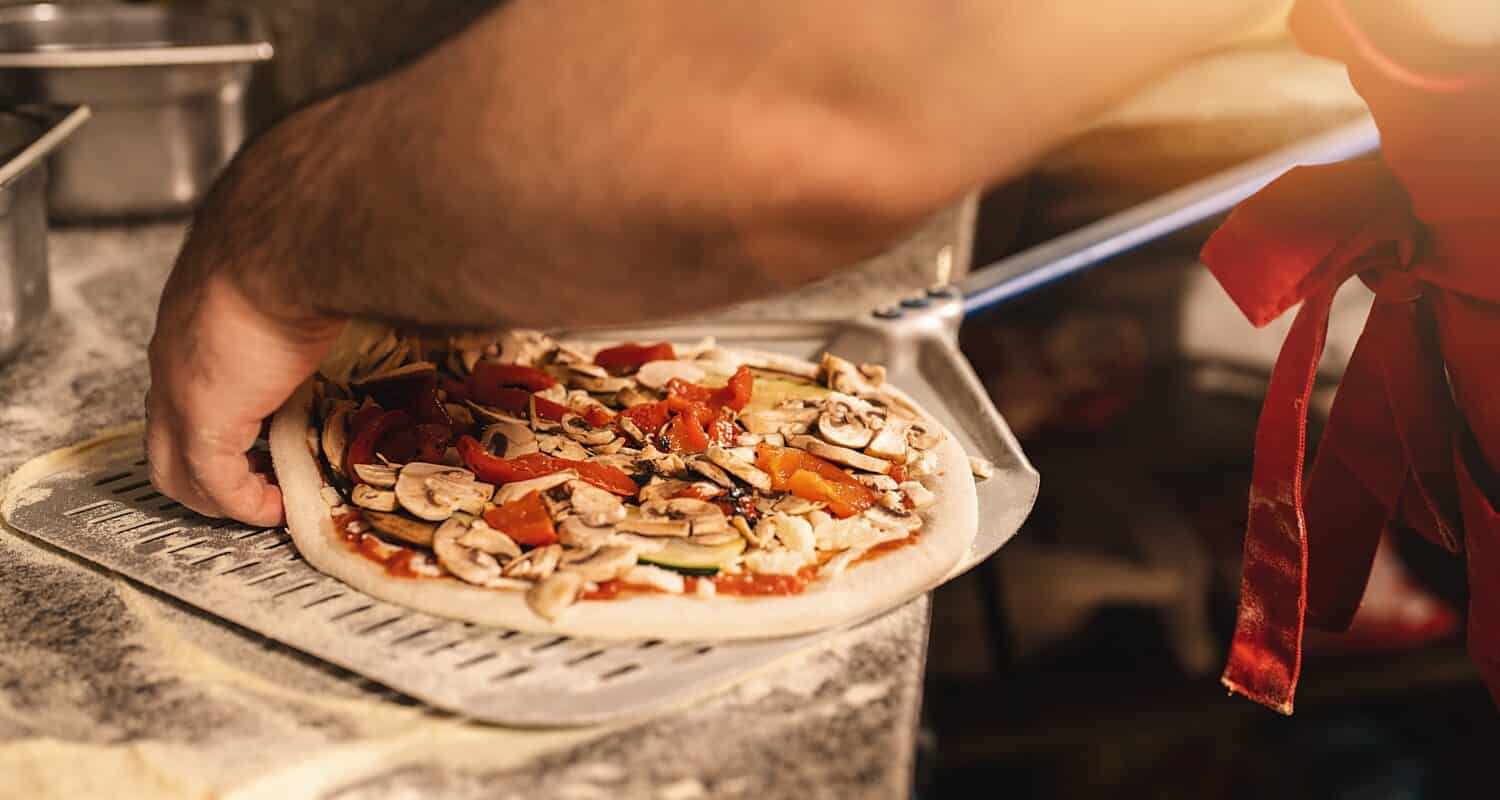 italian pizza baker prepäring fresh pizza on peel at pizzeria