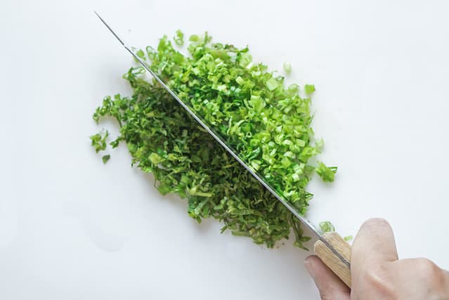 Chopping culantro with knife on plastic block