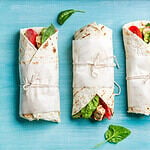 Healthy lunch snack. Tortilla wraps with grilled chicken fillet and fresh vegetables on blue painted wooden background. Top view