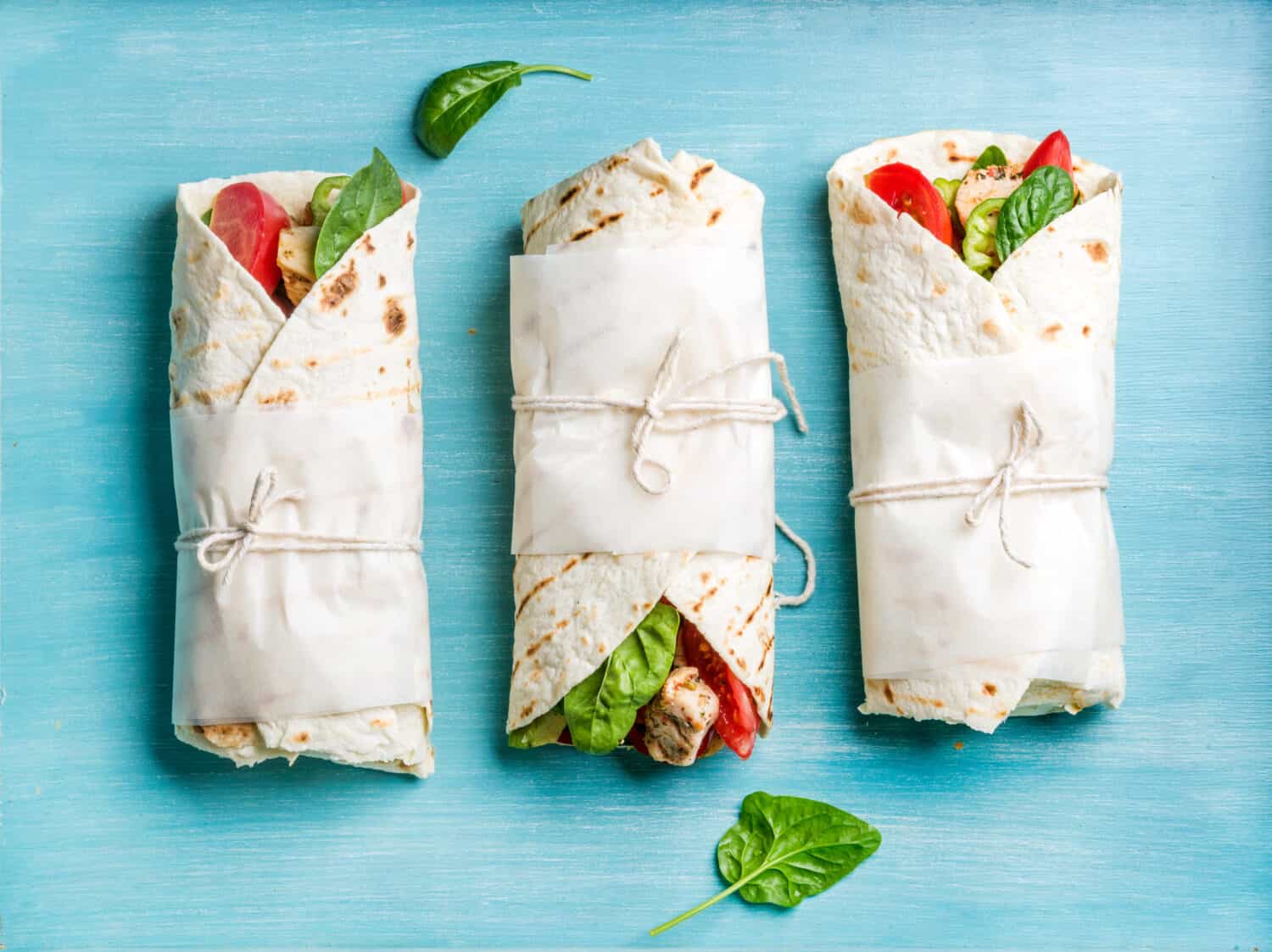 Healthy lunch snack. Tortilla wraps with grilled chicken fillet and fresh vegetables on blue painted wooden background. Top view