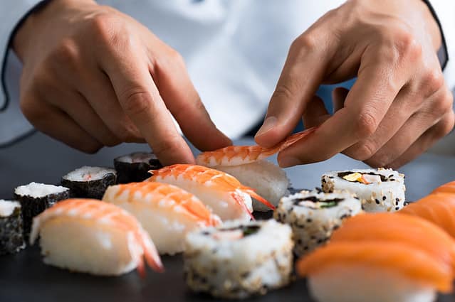 Closeup of chef hands preparing japanese food. Japanese chef making sushi at restaurant. Young chef serving traditional japanese sushi served on a black stone plate.