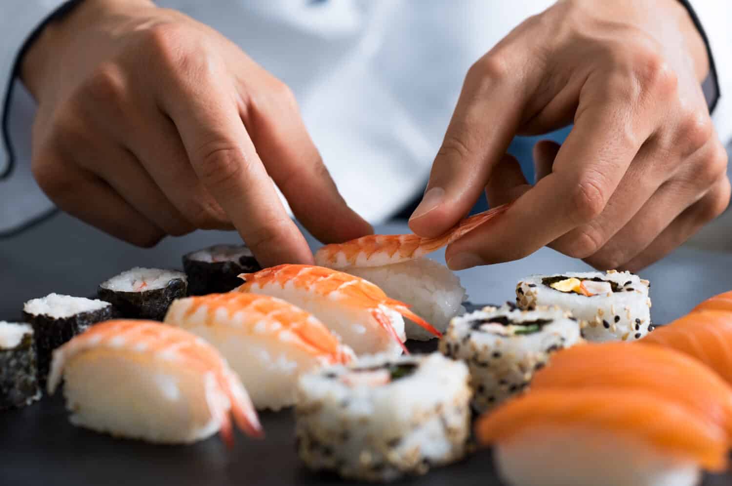 Closeup of chef hands preparing japanese food. Japanese chef making sushi at restaurant. Young chef serving traditional japanese sushi served on a black stone plate.